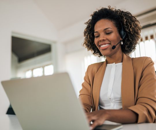 Low angle portrait of a happy woman wearing headset using laptop. Low angle portrait of a happy woman wearing headset using laptop.